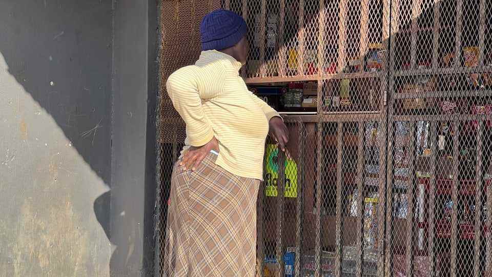 A woman stands in front of a barred neighborhood shop.