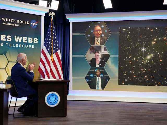 In the foreground on the left, US President Joe Biden is seated in front of a video wall on the right, showing three people and the new image from the space telescope.