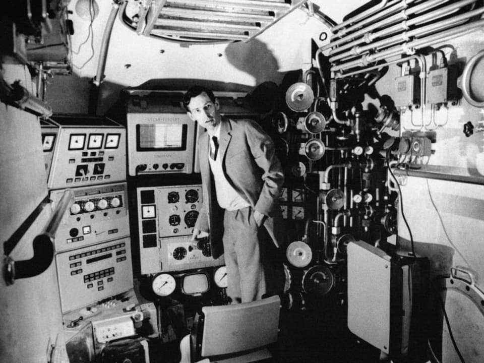 Black and white photo: An elegantly dressed man is standing in the control center of a submarine