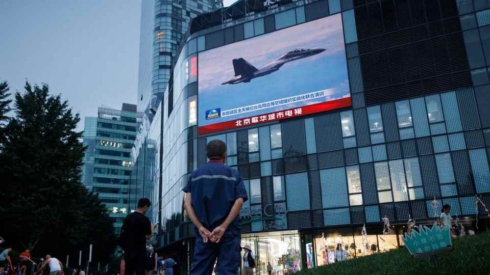 Passerby looks at fighter jet on TV
