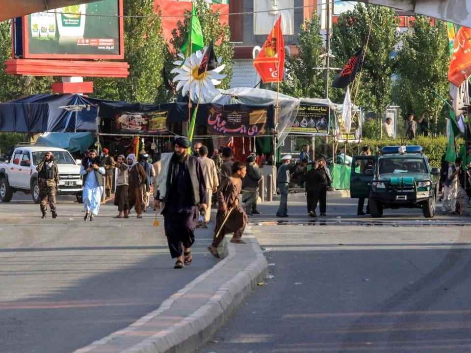 Several people are walking on a street.  There are flags and market stalls at the roadside.
