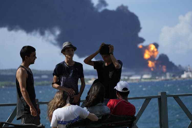 Youth gather on a dock as flames and smoke rise from the supertanker base in Matanzas. 