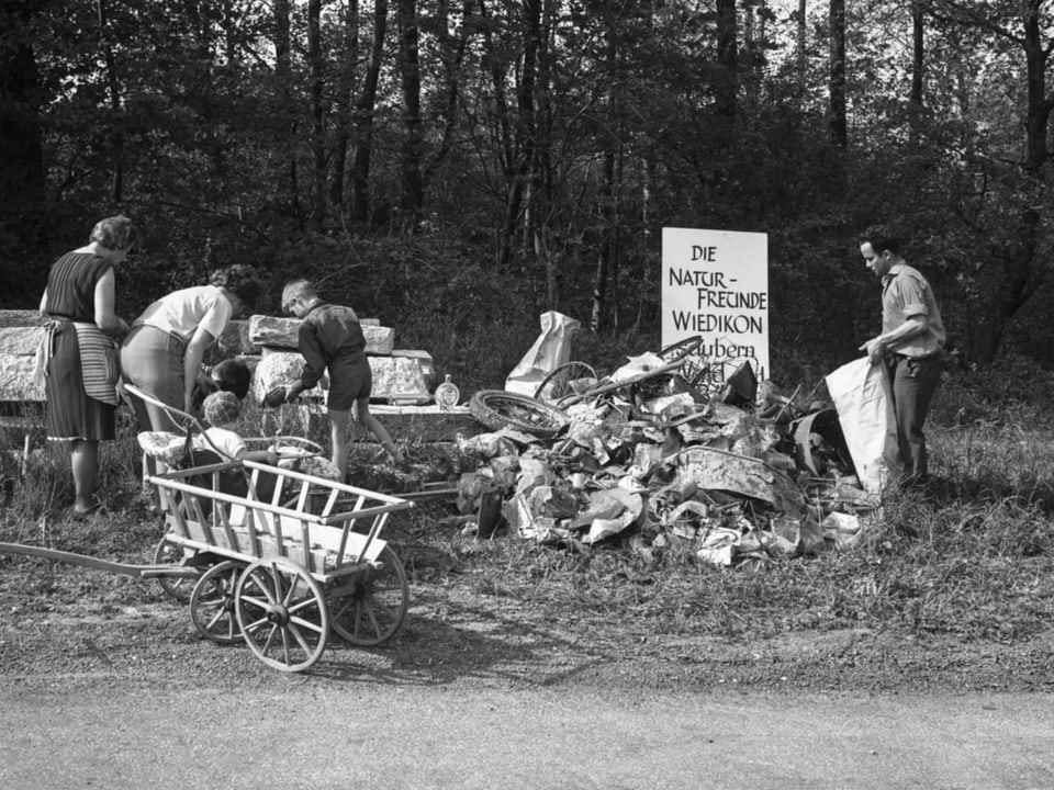 A heap of rubbish, volunteers working in between, carts in the foreground