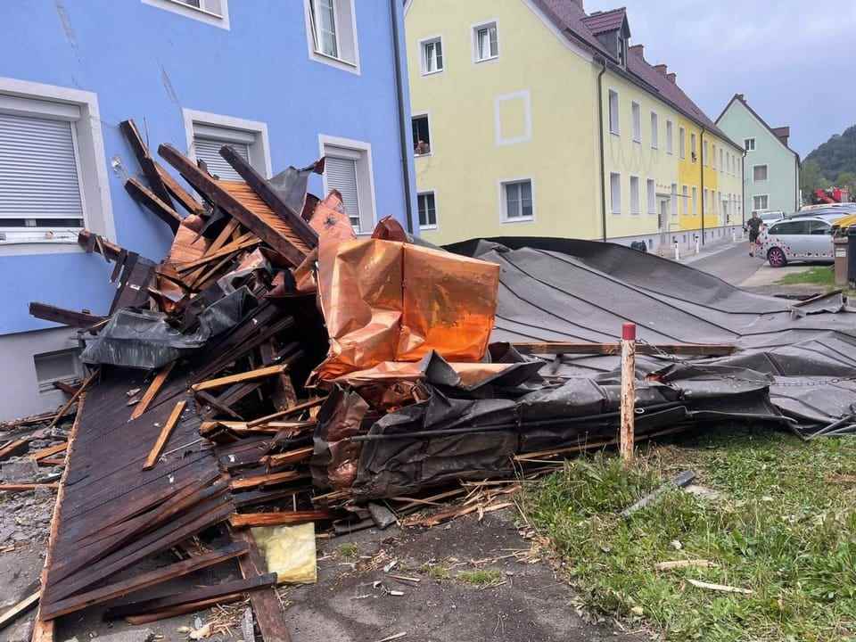 Smashed parts of the roof lie next to a house.