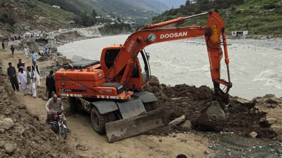 An excavator in Pakistan shovels rocks next to a river.