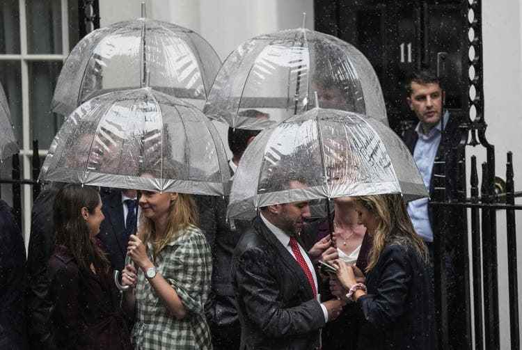Staff and friends of Liz Truss await the arrival of the new Prime Minister at Downing Street in the pouring rain.