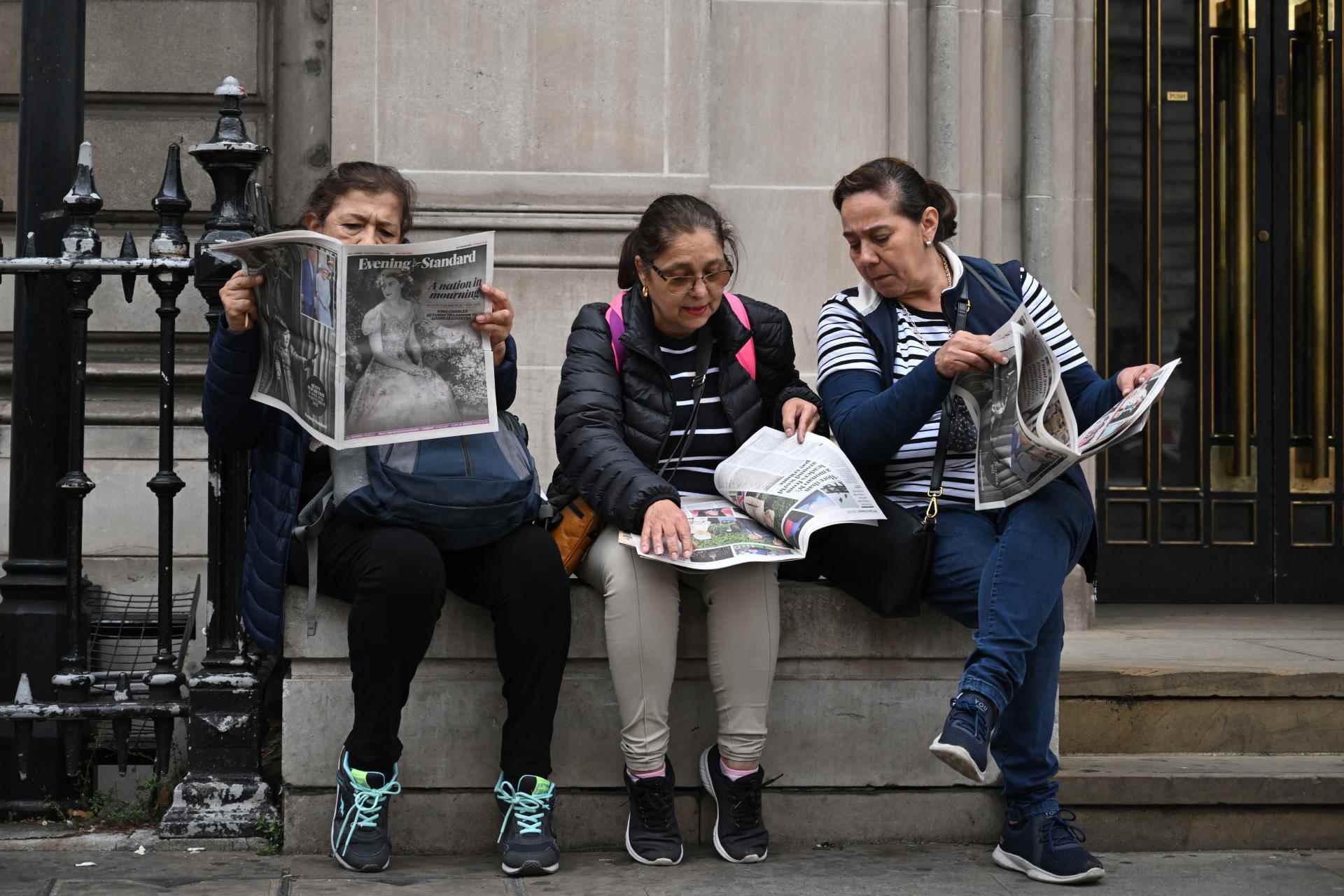 Three tourists read a free London newspaper, 'The Evening Standard', in central London on September 9, 2022.