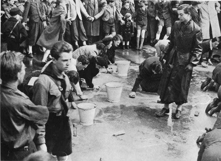 Vienna, 1938: members of the Hitler Youth force Jews to clean the streets while passers-by look on.