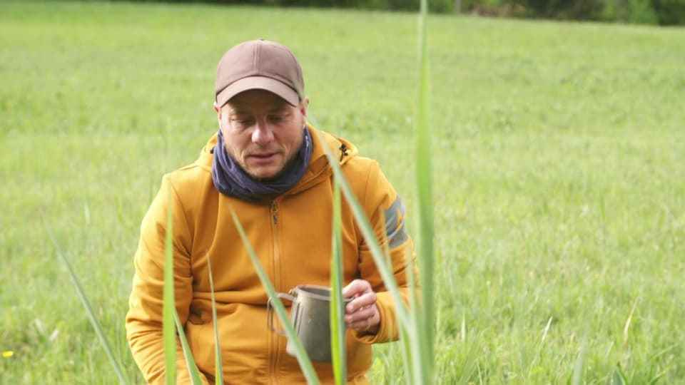 Man in hat and hoodie holding a cup in his hand outdoors.