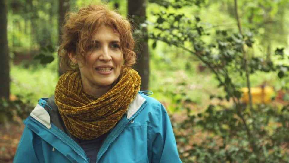 A woman with a scarf and a rain jacket in the forest.