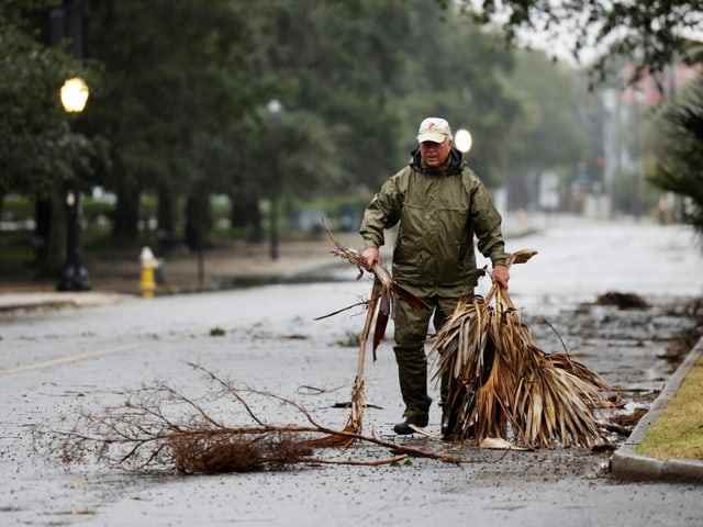 A man walks across a street carrying fallen branches away from there.