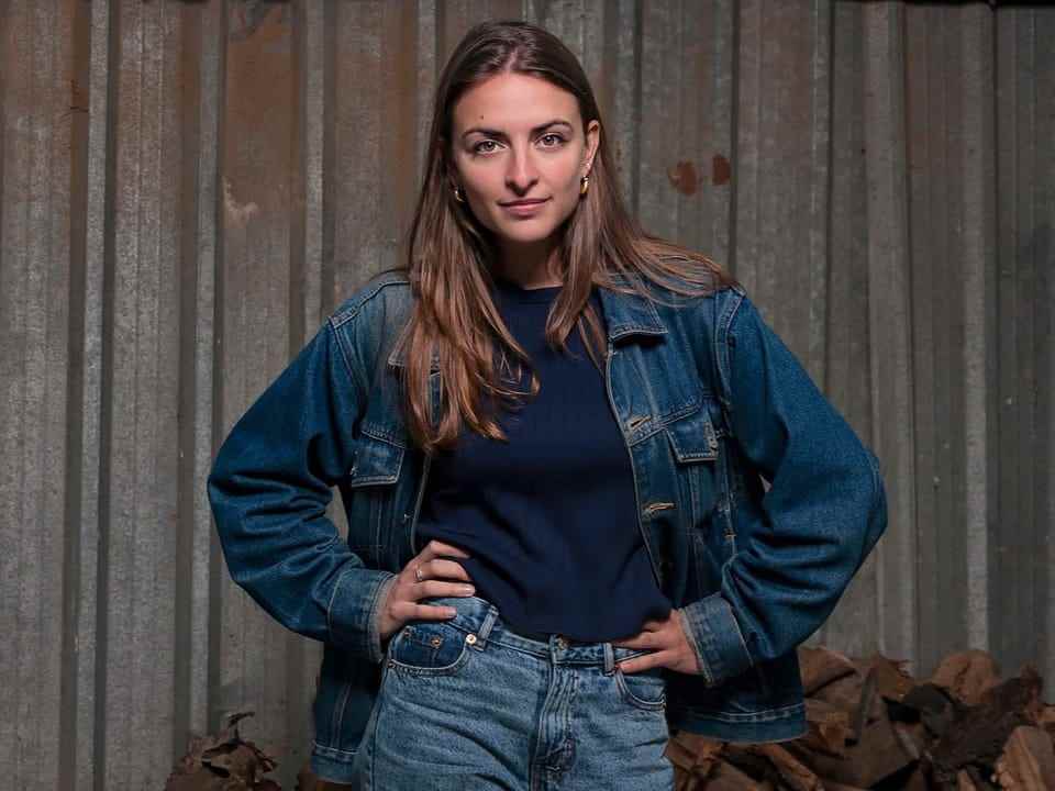Young woman in jeans and denim shirt stands in front of corrugated iron