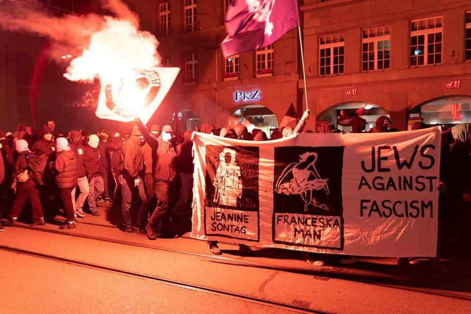 Protesters in the city of Bern, with fire and placards.  Some of them are masked.