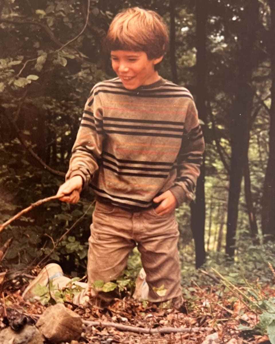 Schoolboy holds a stick for barbecuing in the woods.