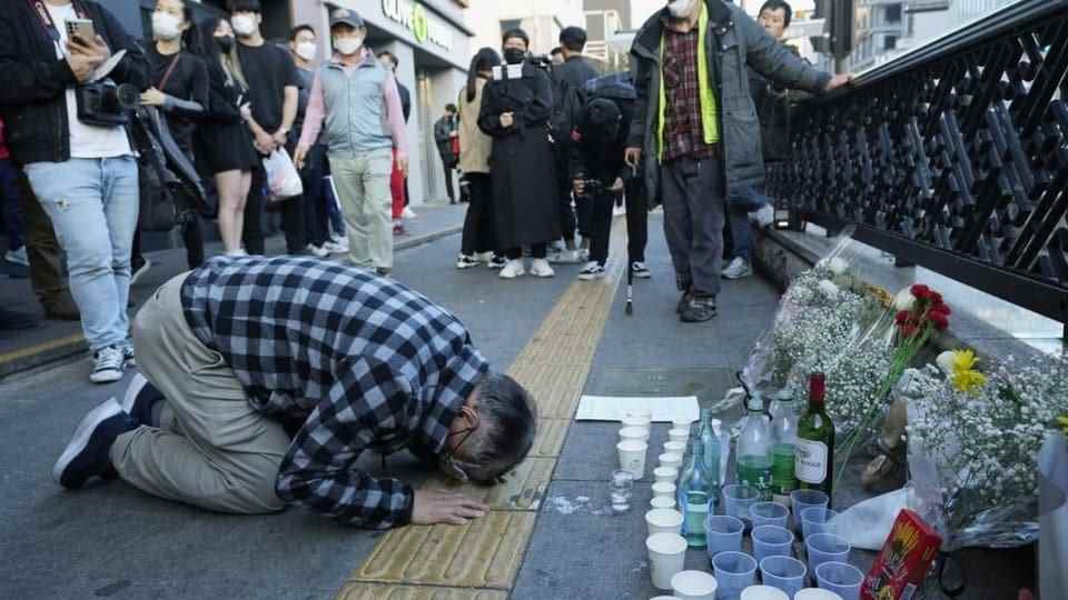 A man kneels in front of a memorial shrine with flowers.
