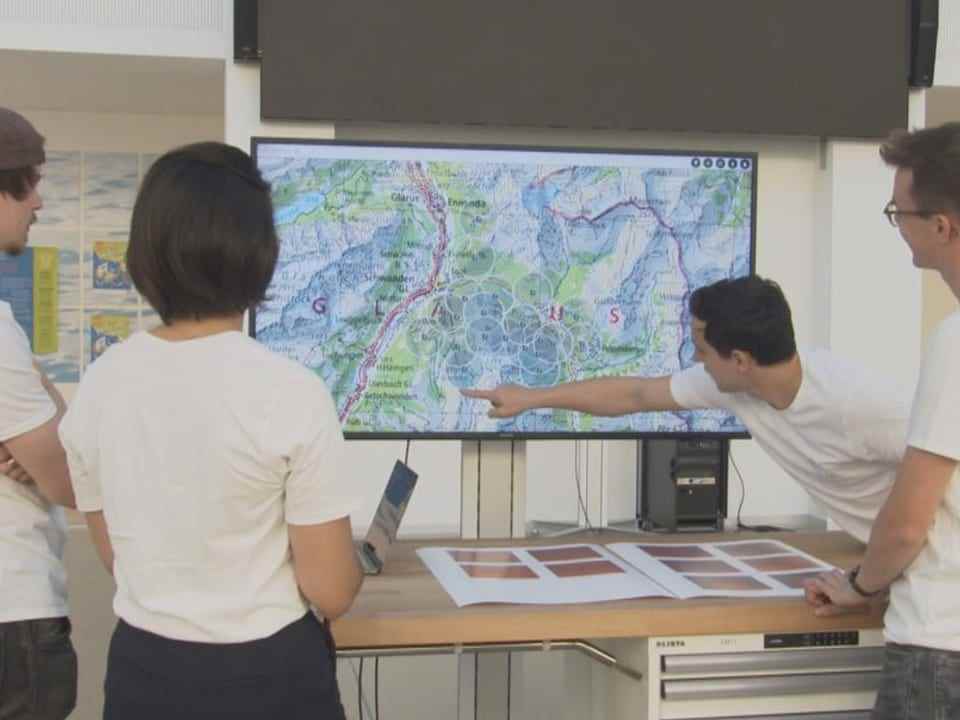Four people in front of a screen showing a map.  Man pointing finger at map