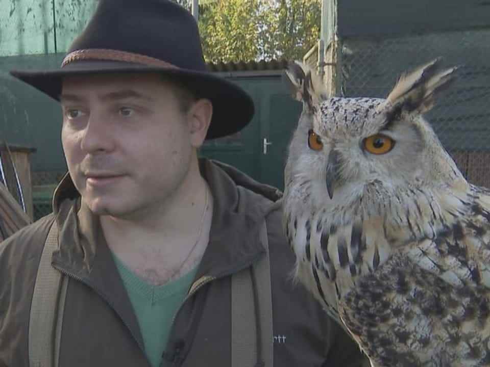 Man in a hat carrying a white owl on his arm