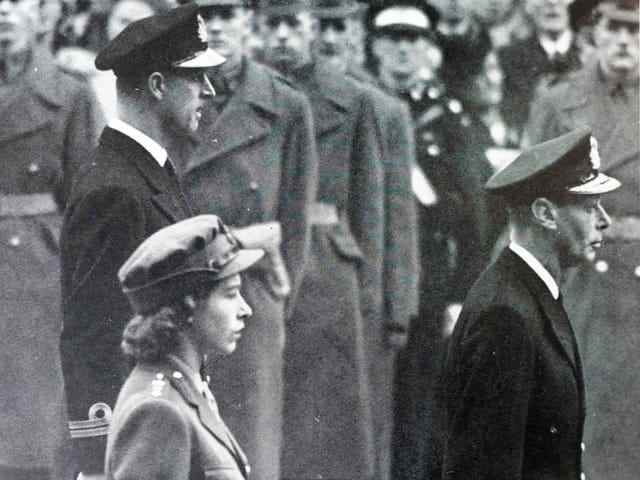 Queen Elizabeth II stands behind her father and next to her husband.