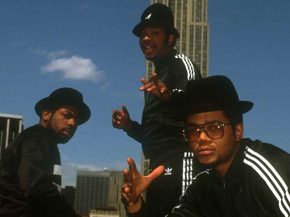 Three young men in black tracksuits pose in front of a skyscraper