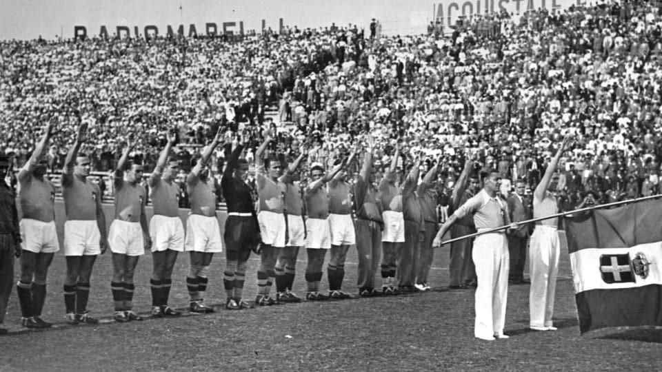 Black and white image: The Italy national football team raises its right hand to the sky.