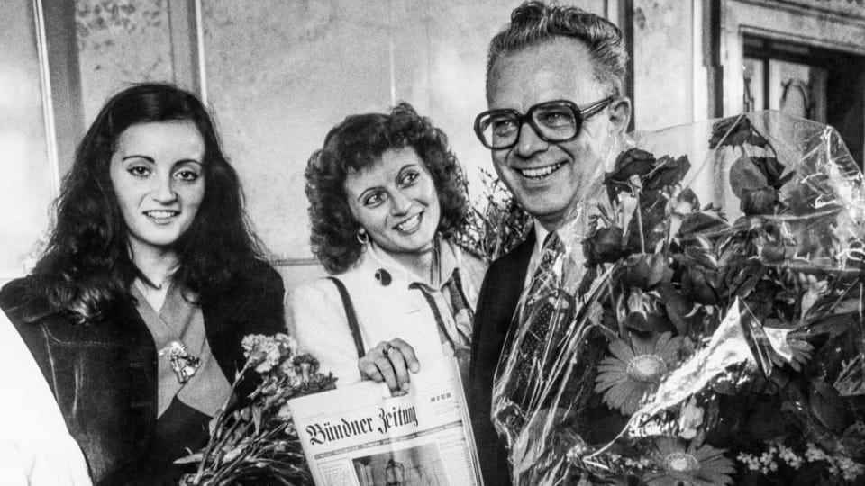 Leon Schlumpf smiles at the camera with his two daughters, holding a bouquet of flowers in his hand.