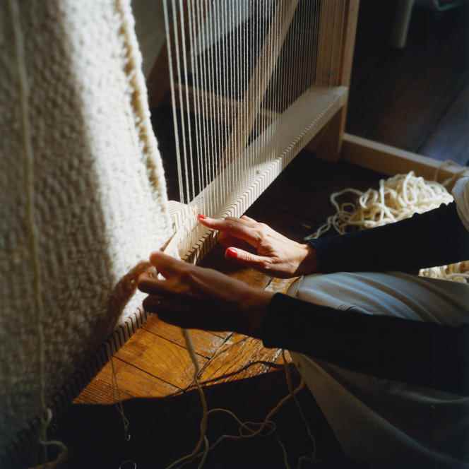 The artist weaves in passing the wooden needle, threaded with wool, above and below the warp threads stretched vertically.