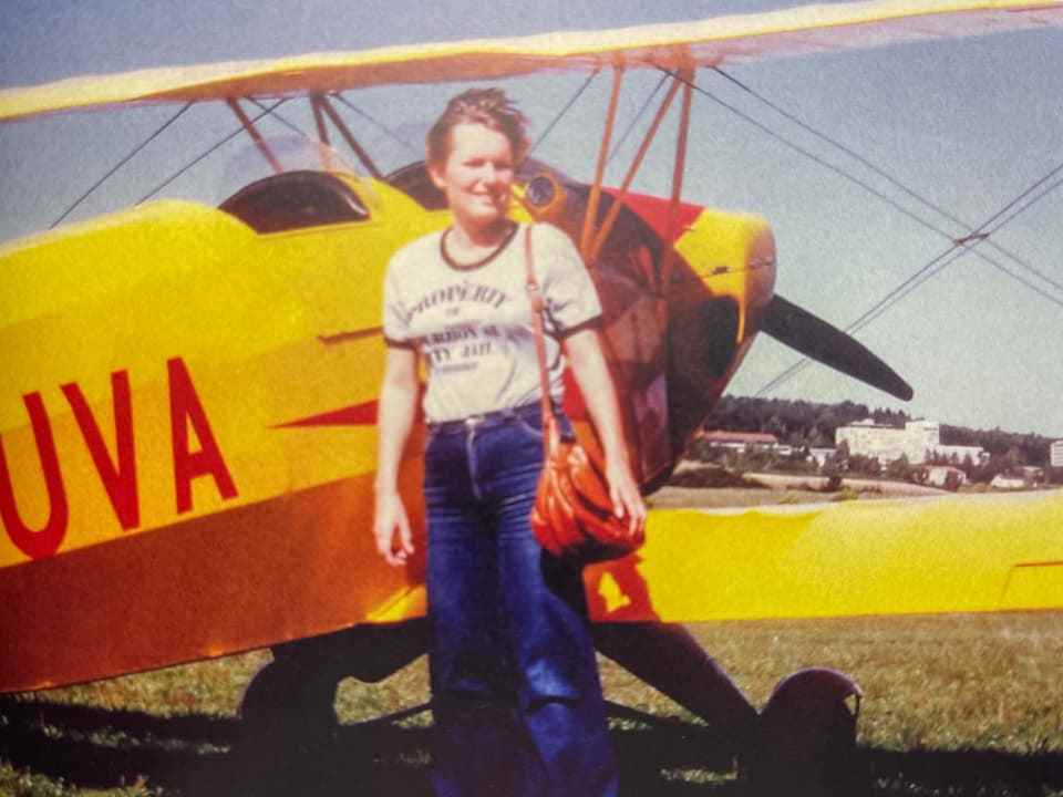 Photograph of a young woman standing in front of an airplane.