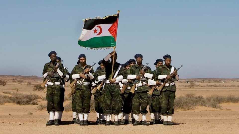 A group of military-clad men with weapons and the flag of Western Sahara