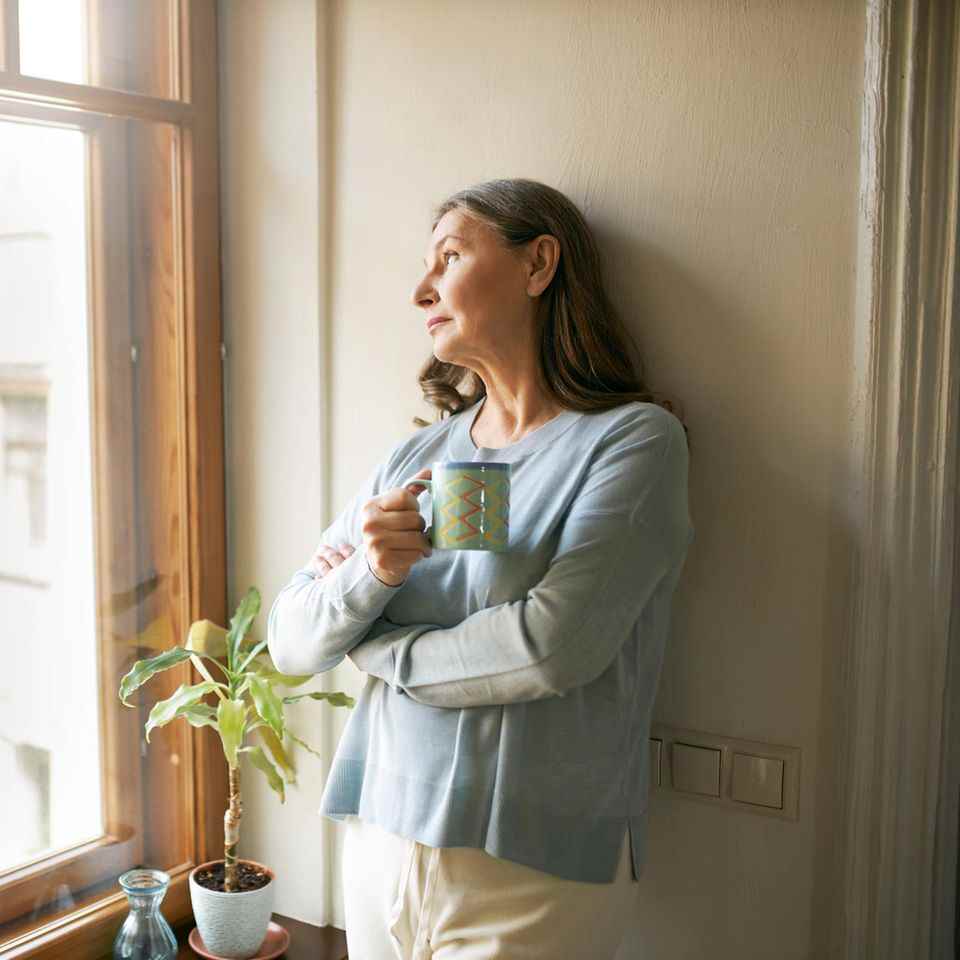 These 6 foods can make menopause worse: Woman looks out the window with cup in hand.