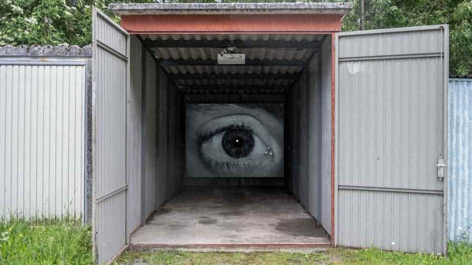 A large eye on the back wall of an open container, the eye is filmed in black and white.