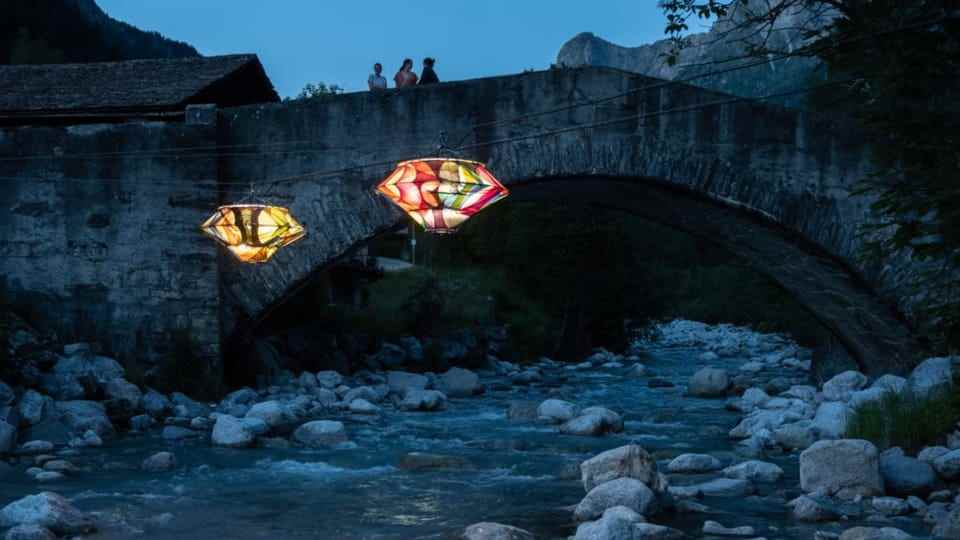 dark river, two colourful, luminous lanterns in front of a stone bridge.