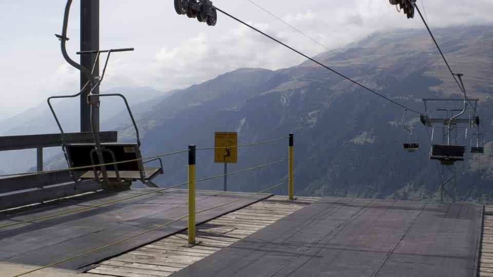 Two empty chairlifts, a mountain peak can be seen in the background.