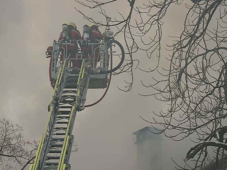 Two firefighters are standing on the fire-fighting ladder, surrounded by a lot of smoke. 