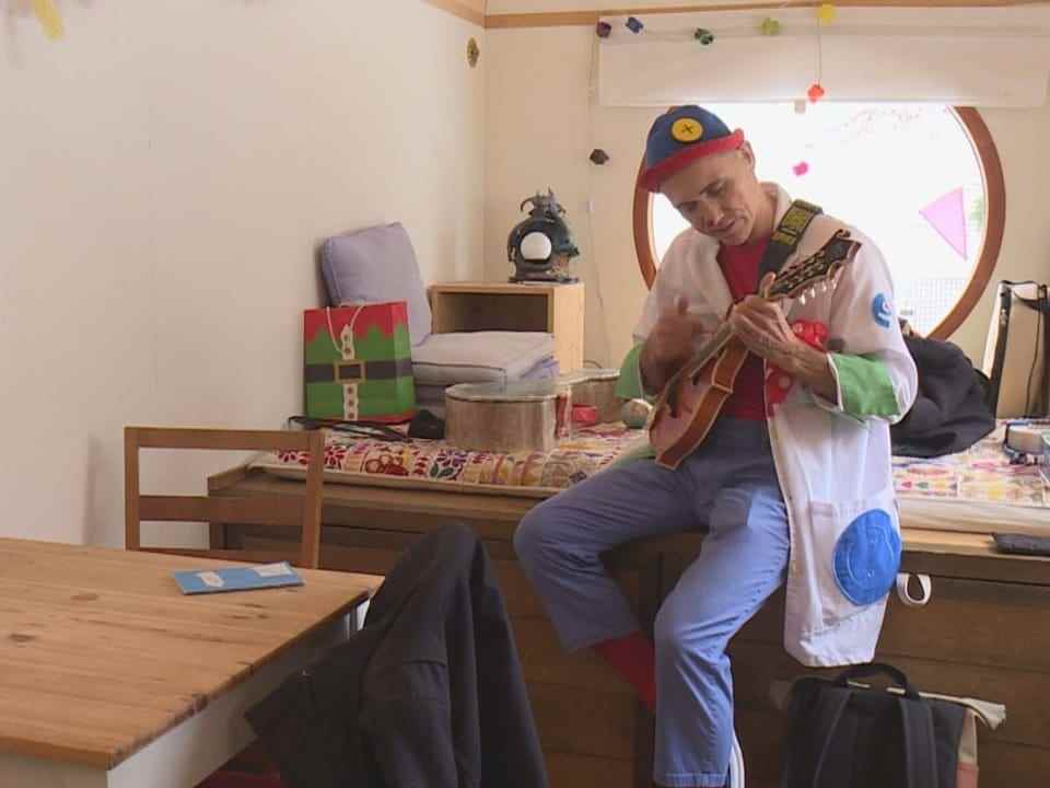 Man dressed as a clown plays a small guitar.