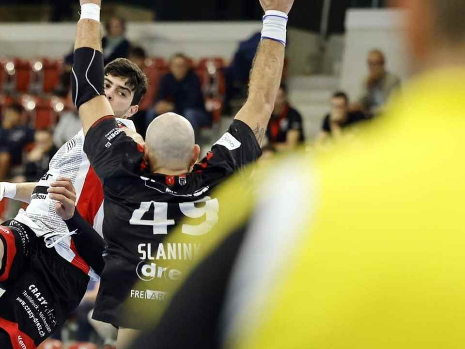 Two handball players in a duel, watched by the referee.