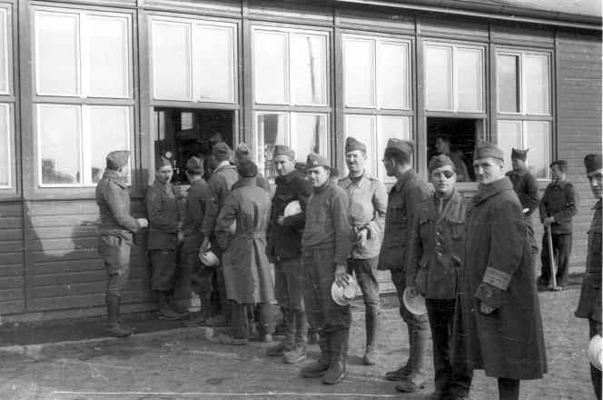 French prisoners of war distribute meals at the barrack where the kitchen is located, November 15, 1940, at the Lichterfelde camp.  The man with the armband (second from the right) is part of the camp police.