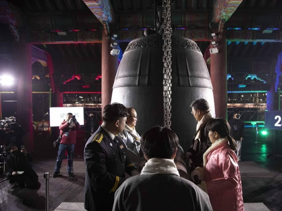 People stand in front of a big bell.