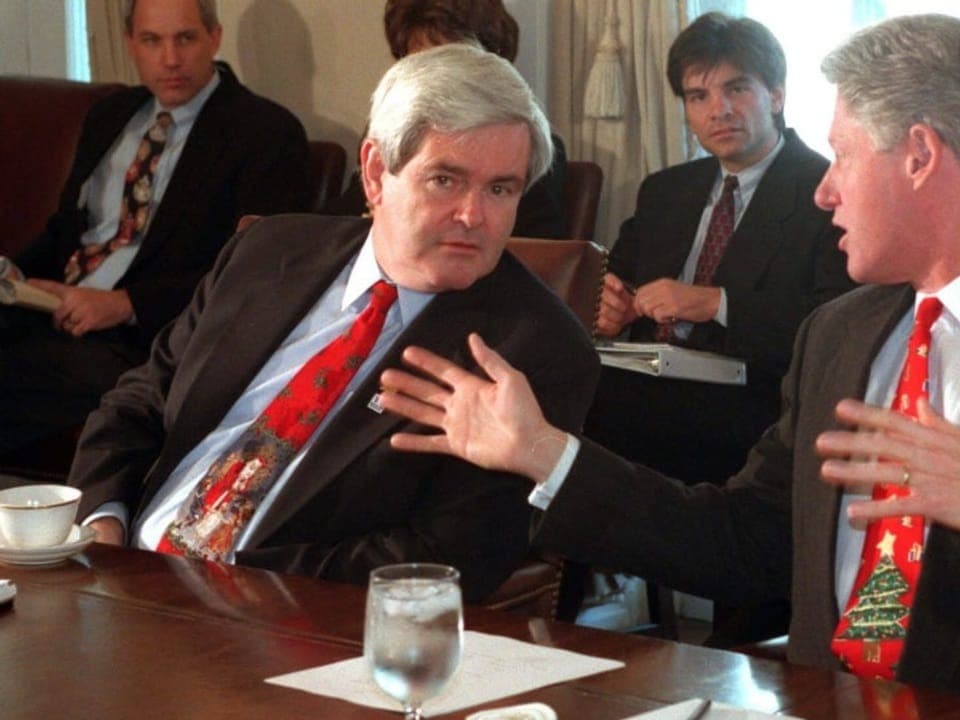 Newt Gingrich and Bill Clinton sit next to each other at the table and are deep in conversation.