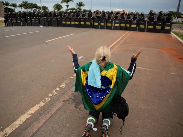A Bolsonaro supporter kneels in front of the advanced security forces.