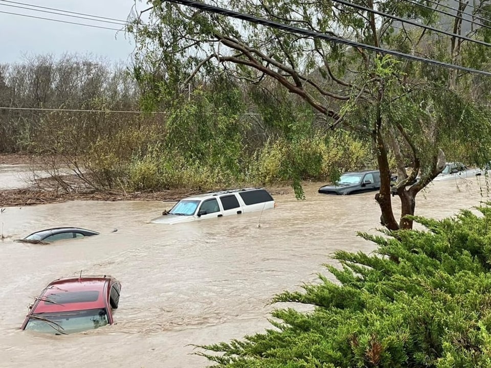 The roofs of washed away cars stick out of the water on a completely flooded street.