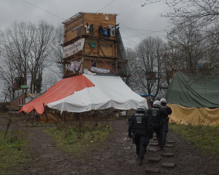 Police officers march through a meadow in Lützerath where demonstrators have built tree houses, huts and a tower.
