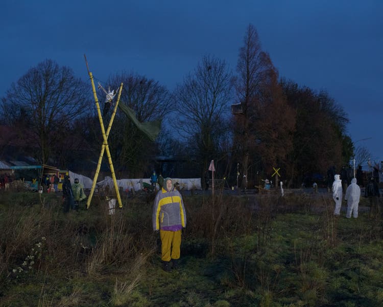 Demonstrators are standing in a field in front of Lützerath, where houses have already been demolished in 2021, and are watching the police.