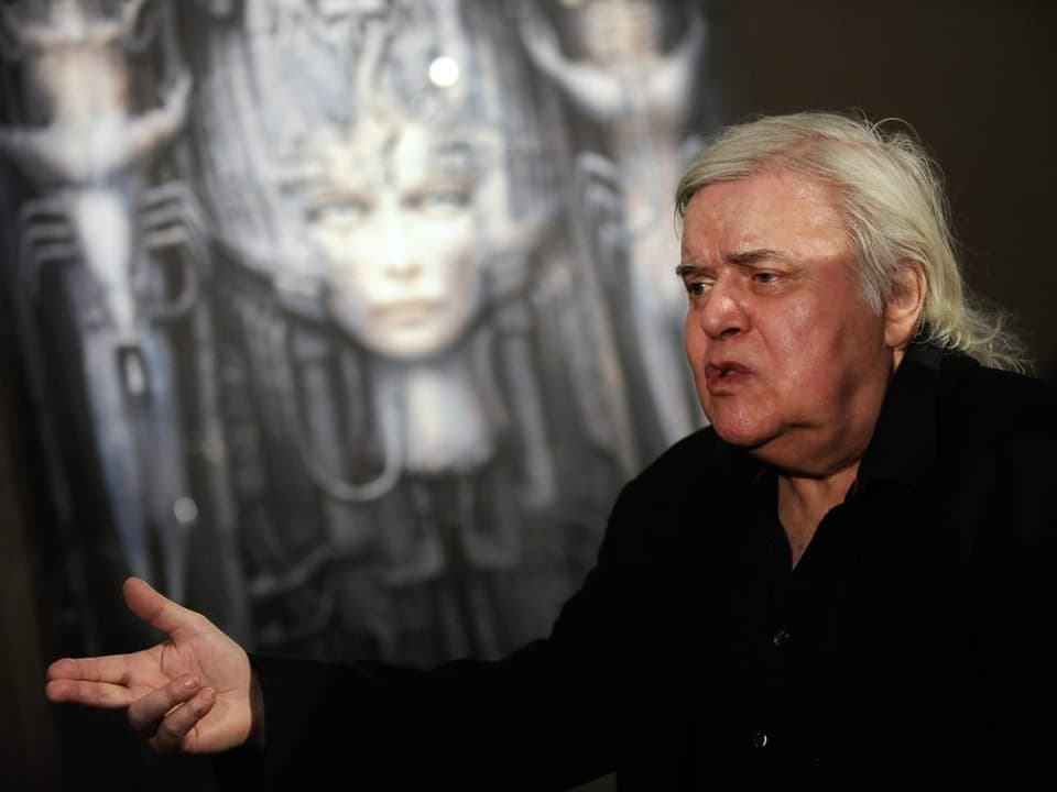 An elderly gentleman with gray hair in front of a picture showing a woman's head.