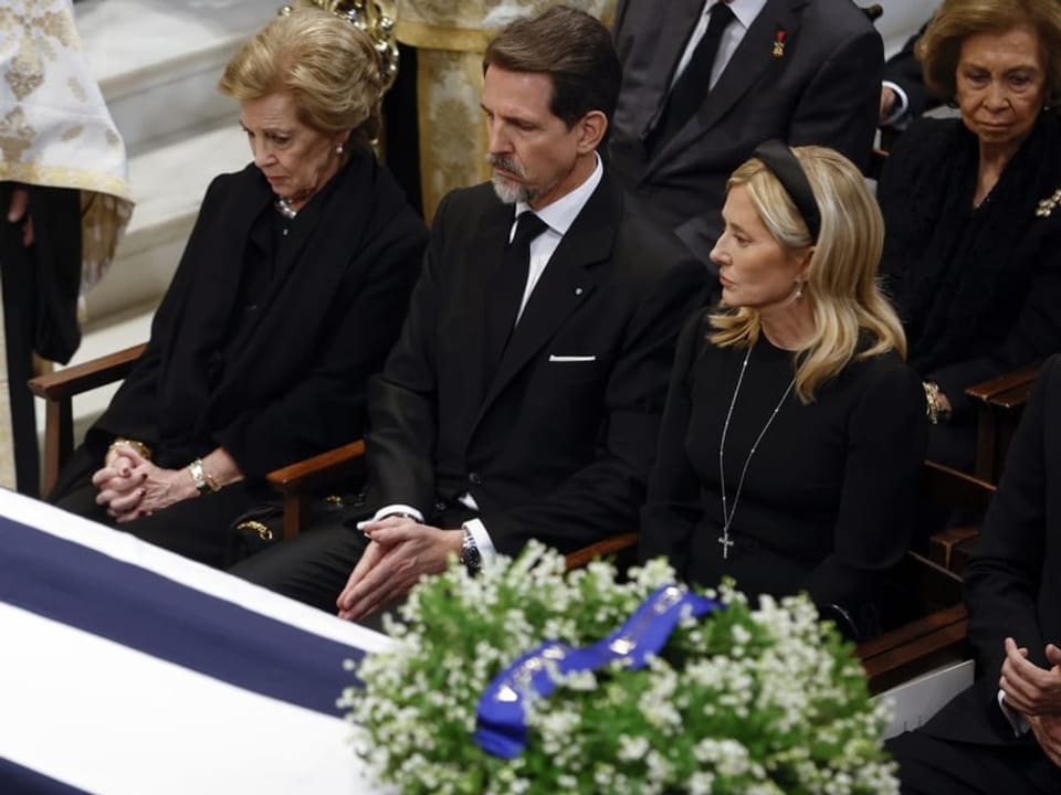 Three people seated next to a coffin.