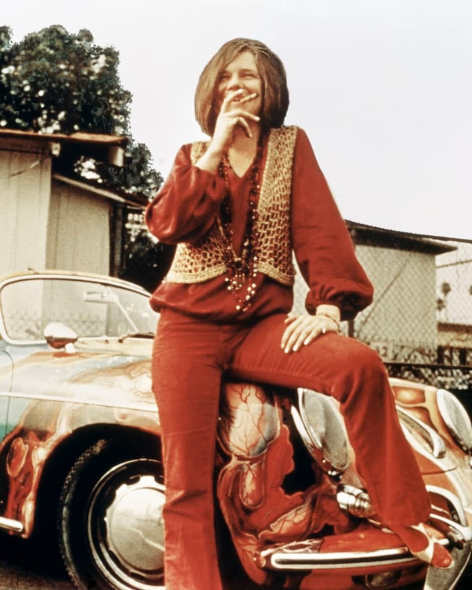 Janis Joplin poses in front of a colorful Porsche.