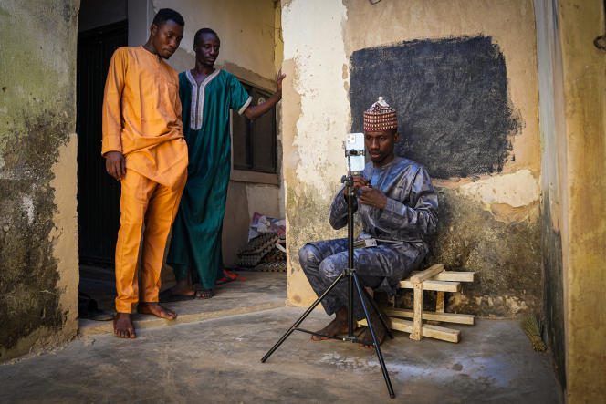 Mubarak Muhammad, aka Unique Pikin, sets up his phone to shoot a video in the courtyard of his house in the city of Kano, as his two brothers look on, in December 2022.