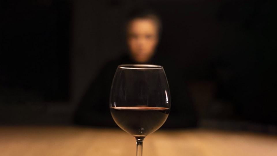 front in focus.  A glass of red wine.  A blurred face in front of a black background.