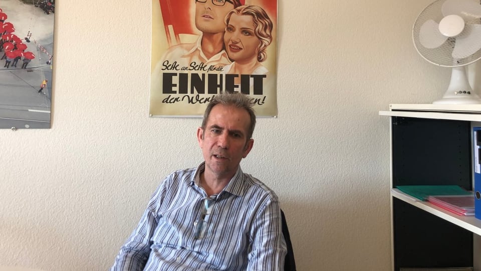 Hilmi Gashi in front of a historic May Day poster in the office of the Unia trade union 