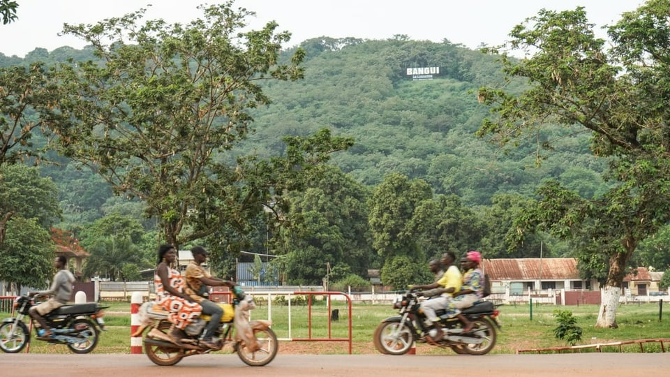 Motorcyclists in front of a hill with the lettering 
