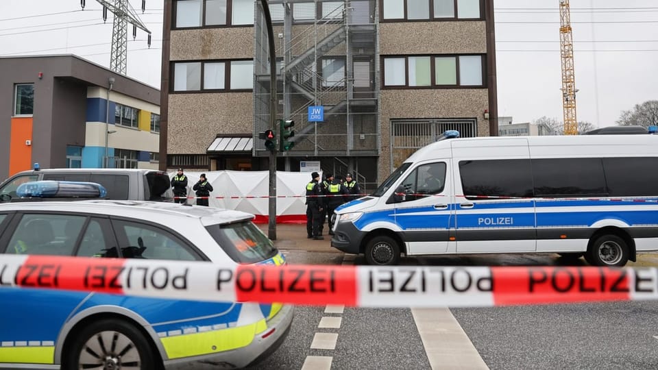Police barrier tape, police vehicles and emergency services stand in front of a building with the inscription 